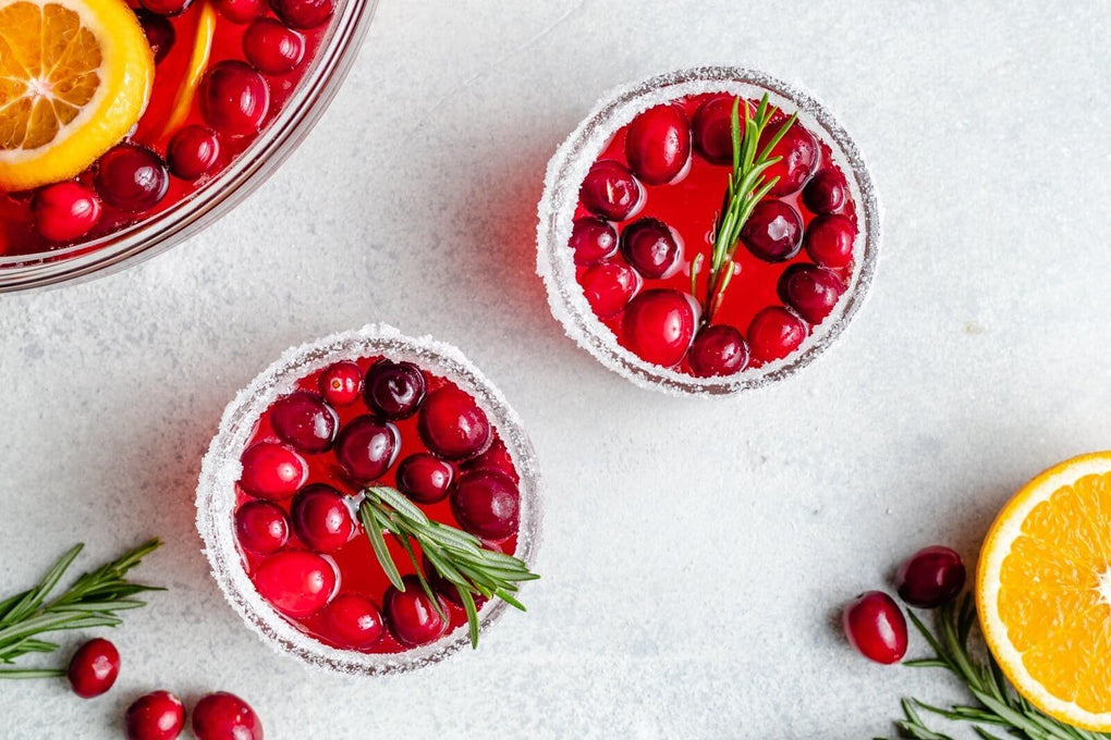 Glass of Holiday Punch cocktail garnished with real cranberries and sprig of rosemary